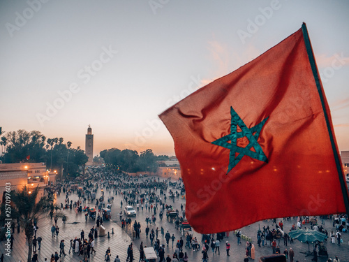 Fotografie The waving flag of Morocco and the famous minaret of Marrakech at sunset