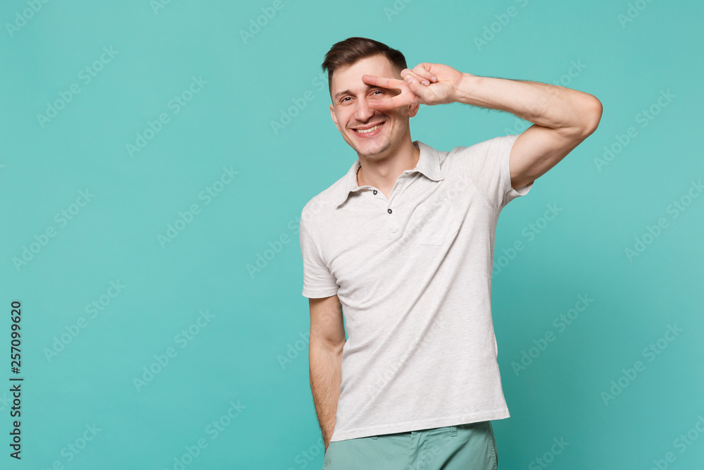 Portrait of cheerful handsome young man in casual clothes showing victory sign isolated on blue turquoise wall background in studio. People sincere emotions, lifestyle concept. Mock up copy space. Portrait of cheerful handsome young man in casual clothes showing victory sign isolated on blue turquoise wall background in studio. People sincere emotions, lifestyle concept. Mock up copy space.
