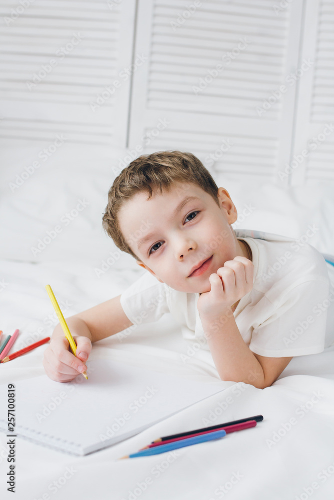 Boy draws with colorful pencils sitting on the bed Boy draws with colorful pencils sitting on the bed