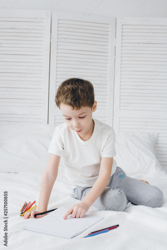 Boy draws with colorful pencils sitting on the bed Boy draws with colorful pencils sitting on the bed