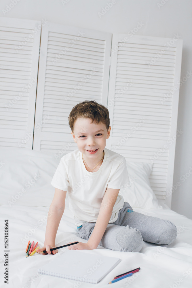 Boy draws with colorful pencils sitting on the bed Boy draws with colorful pencils sitting on the bed