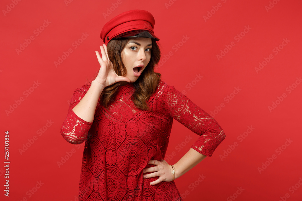 Portrait of amazed young woman in lace dress, cap looking camera, whispering secret behind her hand isolated on red background in studio. People sincere emotions lifestyle concept. Mock up copy space. Portrait of amazed young woman in lace dress, cap looking camera, whispering secret behind her hand isolated on red background in studio. People sincere emotions lifestyle concept. Mock up copy space.