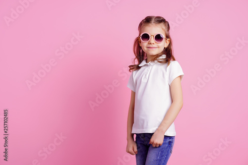 Portrait of beautiful smiling cute model in trendy round sunglasses. Casual 7 y.o. girl posing isolated on pink background. © zamuruev