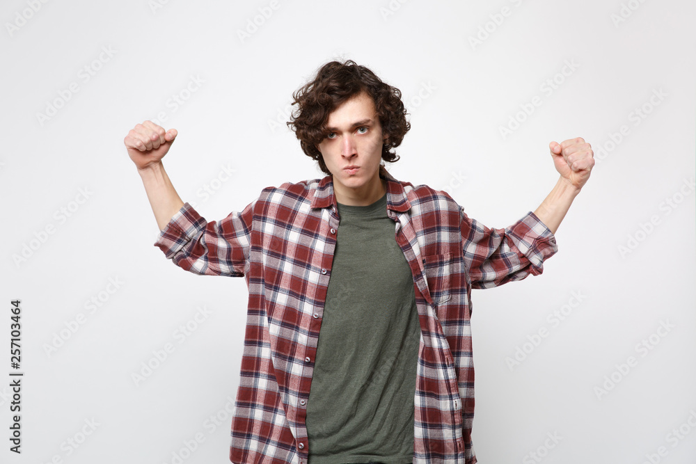Portrait of strong young man in casual clothes looking camera, showing biceps, muscles isolated on white wall background in studio. People sincere emotions, lifestyle concept. Mock up copy space. Portrait of strong young man in casual clothes looking camera, showing biceps, muscles isolated on white wall background in studio. People sincere emotions, lifestyle concept. Mock up copy space.