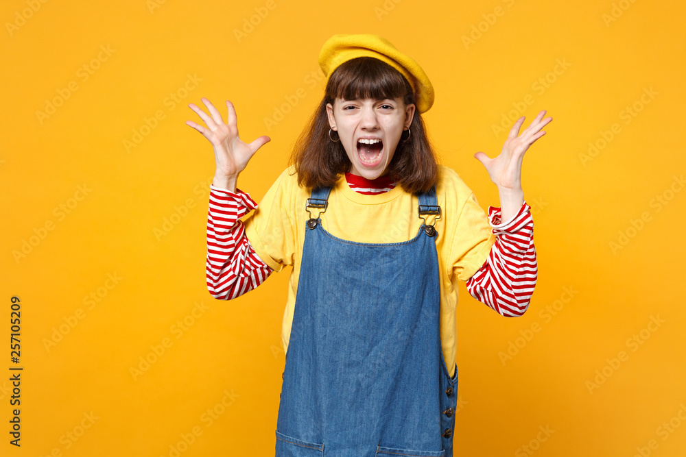 Portrait of crazy screaming girl teenager in french beret, denim sundress spreading hands isolated on yellow wall background in studio. People sincere emotions, lifestyle concept. Mock up copy space. Portrait of crazy screaming girl teenager in french beret, denim sundress spreading hands isolated on yellow wall background in studio. People sincere emotions, lifestyle concept. Mock up copy space.