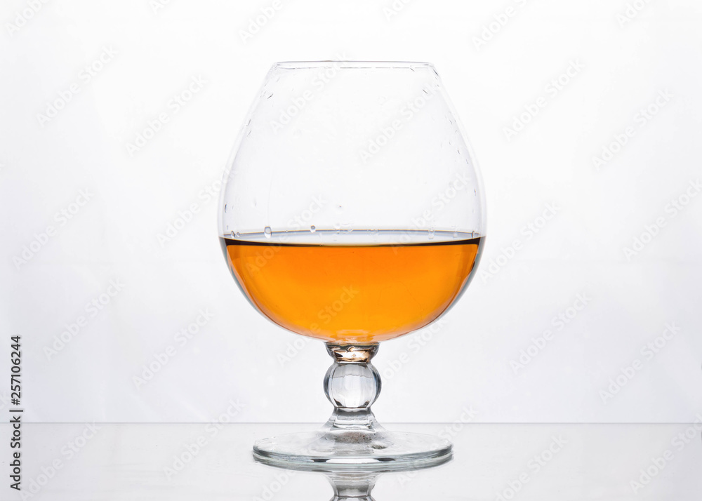 half filled glass with brown cognac on white surface half filled glass with brown cognac on white surface