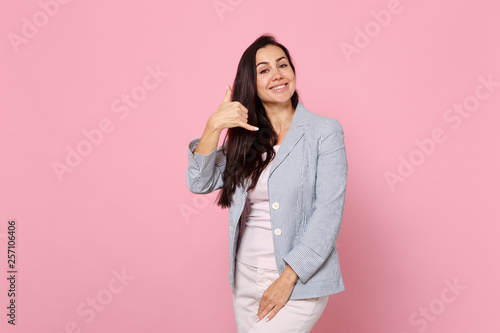 Portrait of smiling young woman in striped jacket doing phone gesture like says call me back isolated on pink pastel wall background. People sincere emotions, lifestyle concept. Mock up copy space. © ViDi Studio