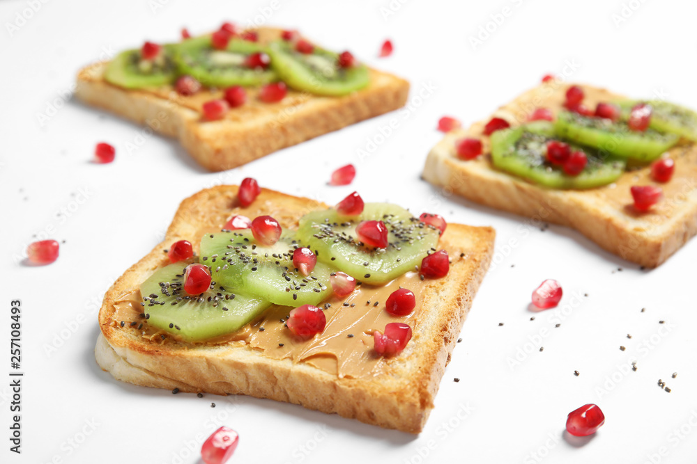 Tasty toasts with kiwi, peanut butter, pomegranate and chia seeds on white background