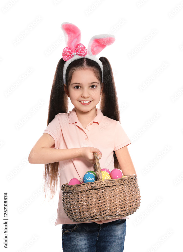 Little girl in bunny ears headband holding basket with Easter eggs on white background