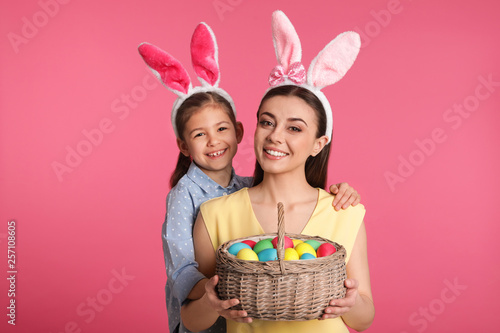Mother and daughter in bunny ears headbands with Easter eggs on color background