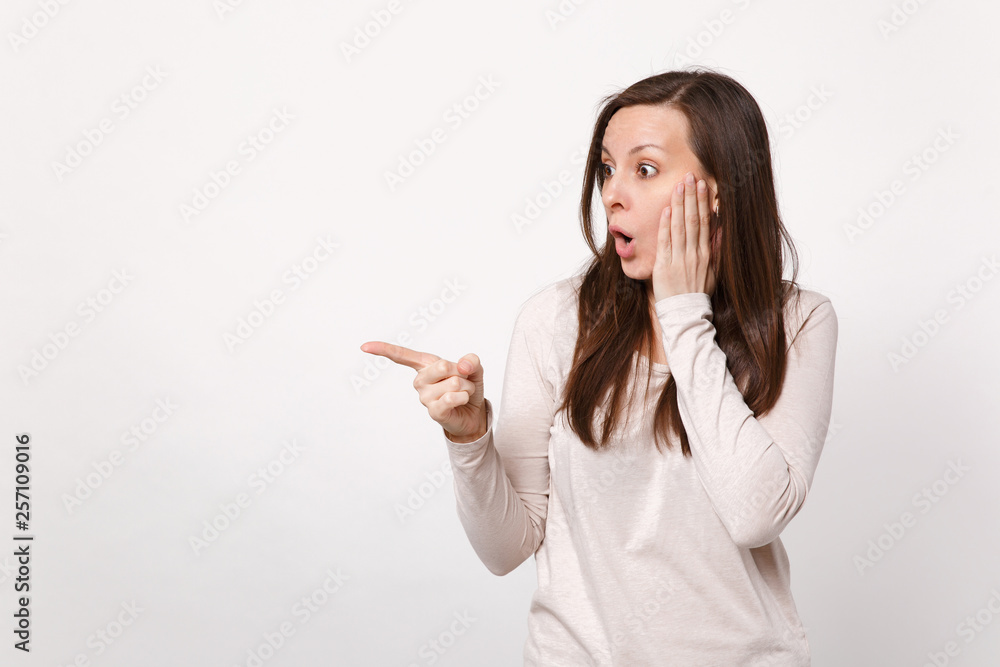 Shocked young woman in light clothes looking aside, putting hand on cheek, pointing index finger isolated on white background in studio. People sincere emotions lifestyle concept. Mock up copy space. Shocked young woman in light clothes looking aside, putting hand on cheek, pointing index finger isolated on white background in studio. People sincere emotions lifestyle concept. Mock up copy space.