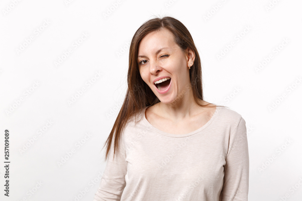 Portrait of funny cheerful smiling blinking brunette young woman in light clothes standing isolated on white background in studio. People sincere emotions, lifestyle concept. Mock up copy space. Portrait of funny cheerful smiling blinking brunette young woman in light clothes standing isolated on white background in studio. People sincere emotions, lifestyle concept. Mock up copy space.