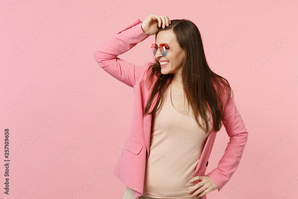 Portrait of smiling young woman in heart glasses putting hand on head, looking aside isolated on pastel pink wall background in studio. People sincere emotions, lifestyle concept. Mock up copy space. Portrait of smiling young woman in heart glasses putting hand on head, looking aside isolated on pastel pink wall background in studio. People sincere emotions, lifestyle concept. Mock up copy space.
