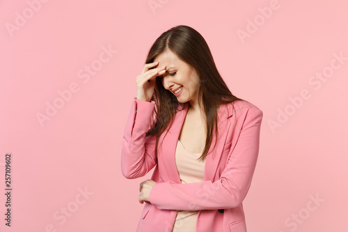 Portrait of displeased crying young woman wearing jacket putting hand on lowered head isolated on pastel pink wall background in studio. People sincere emotions, lifestyle concept. Mock up copy space.