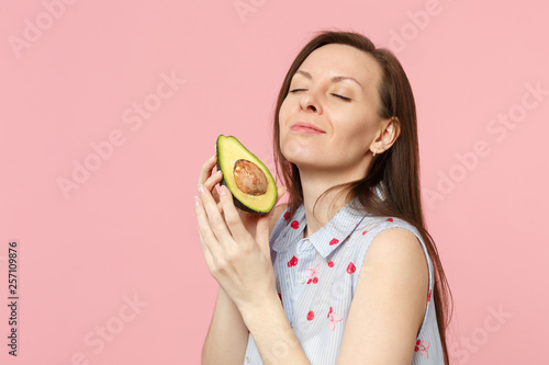 Relaxed young girl in summer clothes keeping eyes clothes hold fresh ripe avocado fruit isolated on pink pastel background in studio. People vivid lifestyle relax vacation concept. Mock up copy space.