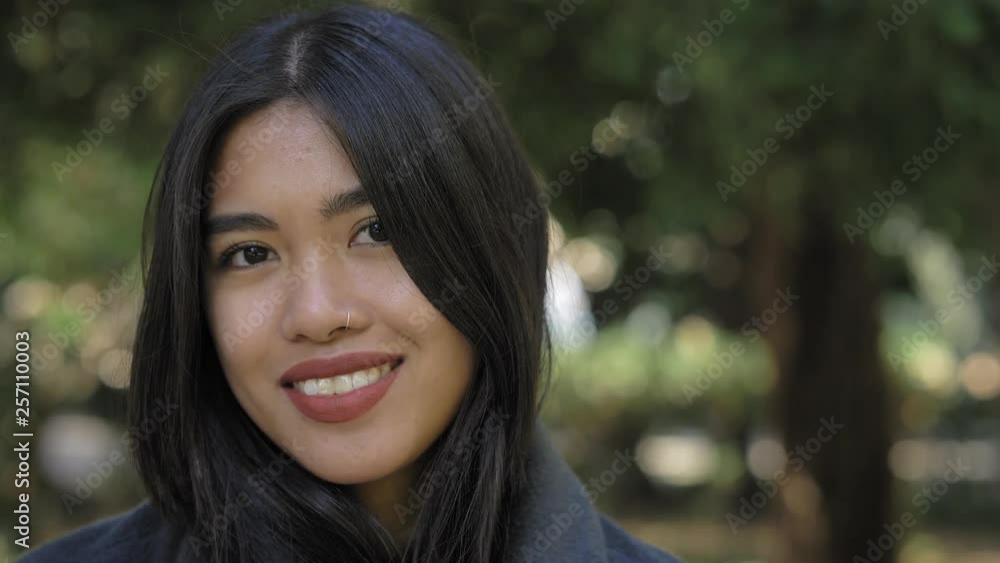 beautiful asian woman smiling on camera in the park with tree in background beautiful asian woman smiling on camera in the park with tree in background