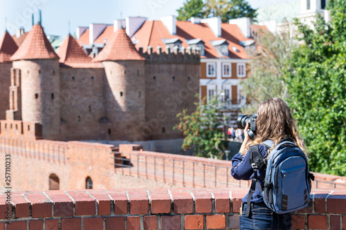 Warsaw, Poland Famous Barbican old town historic city during summer day and red orange brick wall fortress architecture with young woman travel tourist backpack taking picture with camera