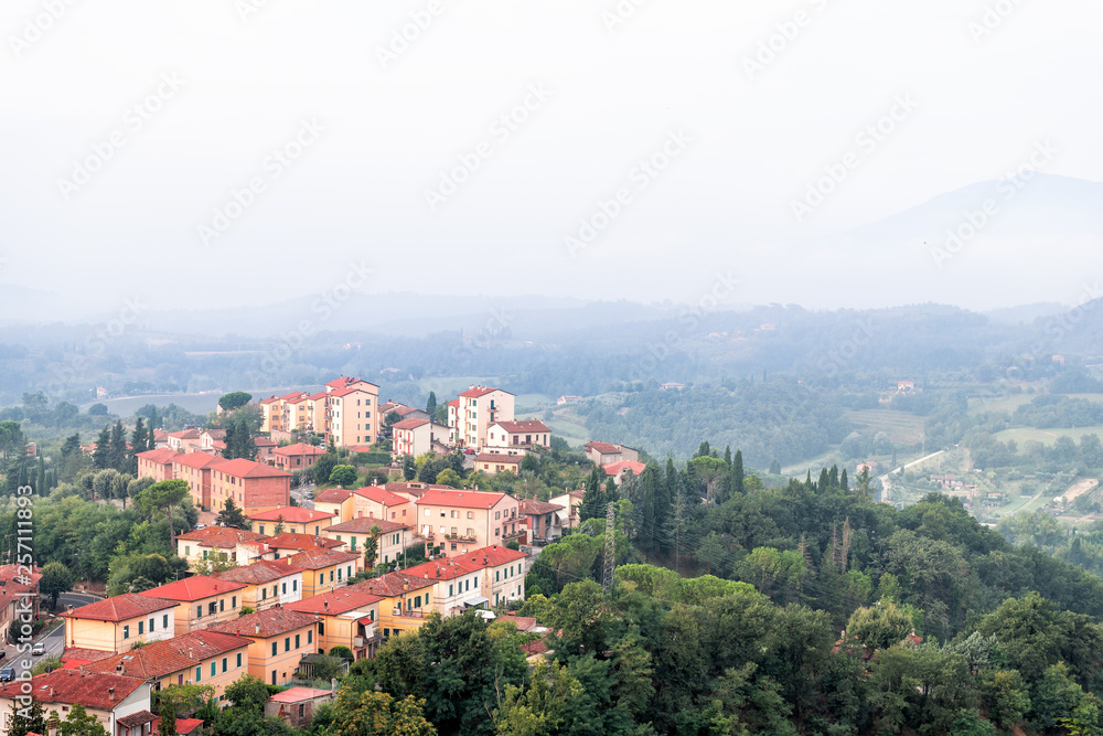 Chiusi village cityscape in Tuscany Italy with orange red rooftop tile houses on mountain countryside and rolling hills with morning mist haze fog