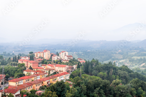 Chiusi village cityscape in Tuscany Italy with orange red rooftop tile houses on mountain countryside and rolling hills with morning mist haze fog