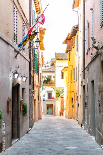 Fototapeta Naklejka Na Ścianę i Meble -  Chiusi, Italy empty street in small town village in Umbria Tuscany narrow vertical view during day with orange pink yellow bright vibrant vivid color walls