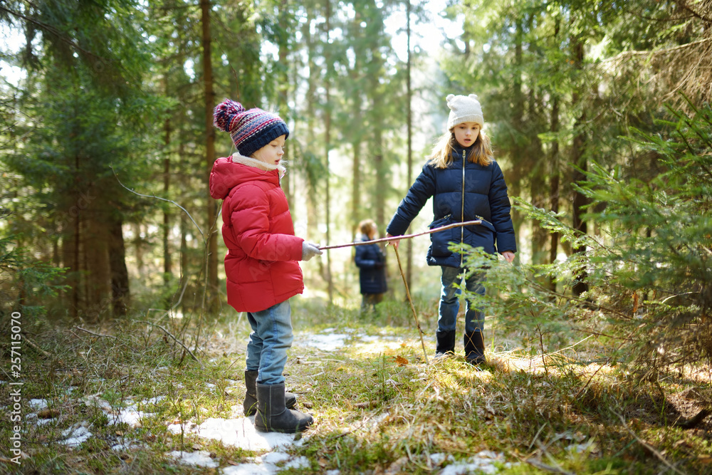 Two cute young sisters having fun during forest hike on beautiful winter day. Active family leisure with kids.