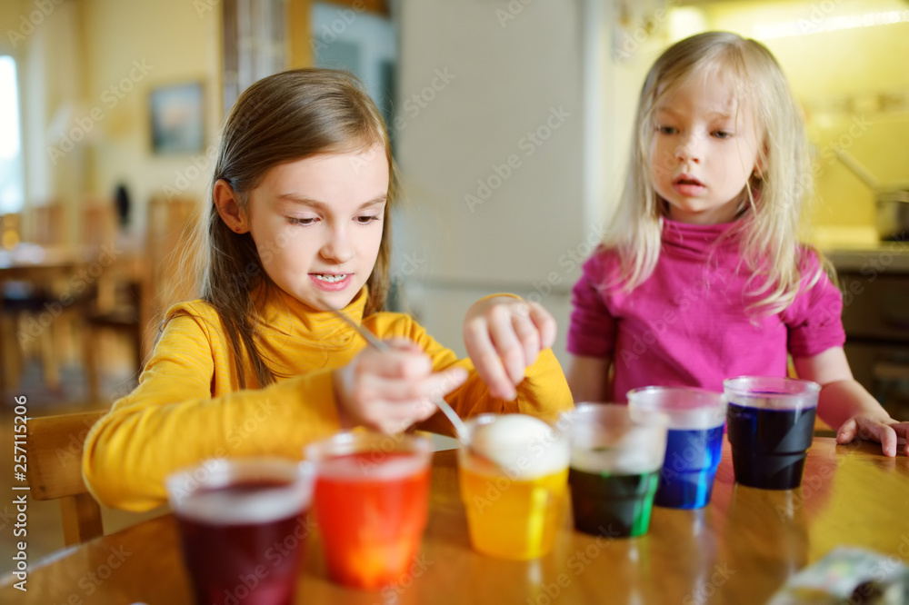 Two cute young sisters dyeing Easter eggs at home. Children painting colorful eggs for Easter hunt. Kids getting ready for Easter celebration. Two cute young sisters dyeing Easter eggs at home. Children painting colorful eggs for Easter hunt. Kids getting ready for Easter celebration.