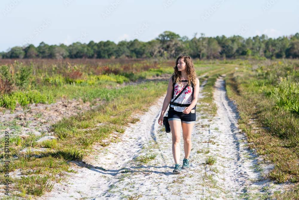 Naklejka premium Woman travel photographer walking on prairie landscape with and trail path in Myakka River State Park Wilderness Preserve in Sarasota, Florida with camera