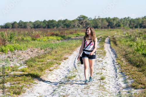 Woman travel photographer walking on prairie landscape with and trail path in Myakka River State Park Wilderness Preserve in Sarasota, Florida with camera photo