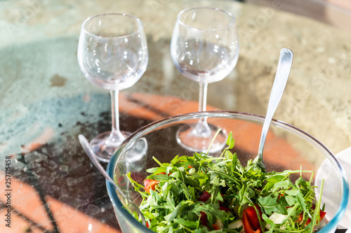 Closeup of fresh raw vegetable salad with arugula greens colorful vibrant healthy lunch meal and two empty wine glasses