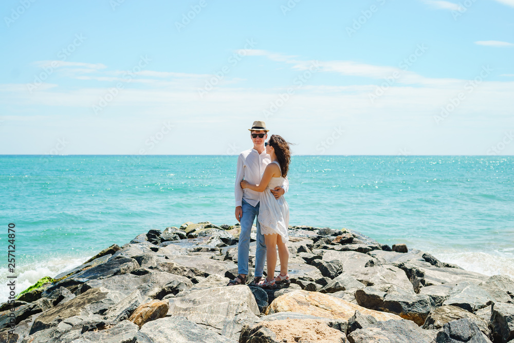 A young couple of lovers, a guy and a girl on the ocean, in white clothes on the stones.