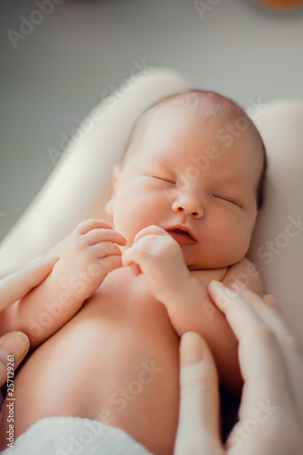 A newborn baby lies on the mother’s lap. Mother holds her newborn baby. Woman relaxing in a white bedroom. Family at home