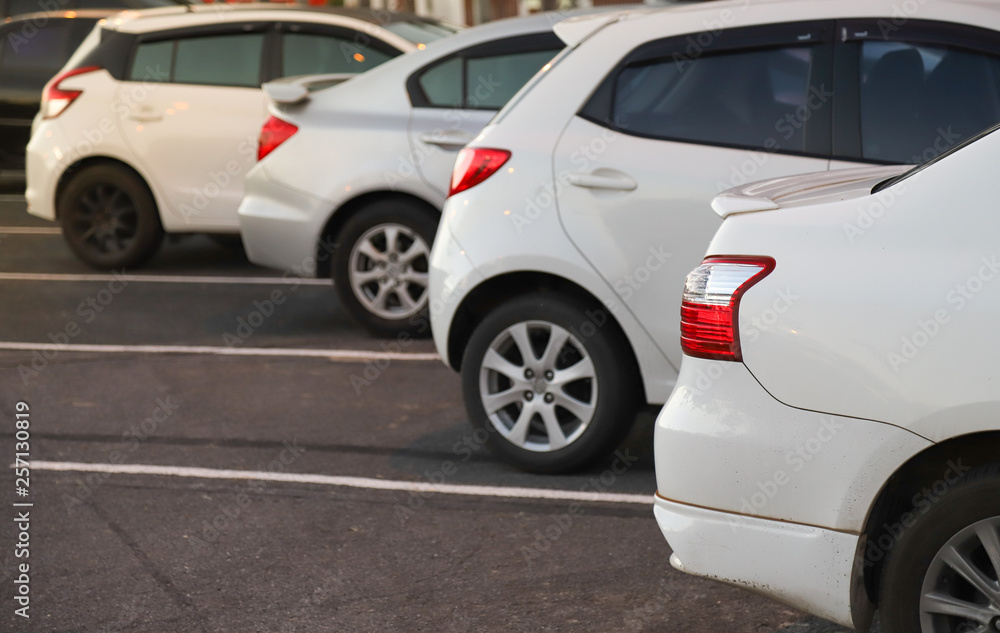 Closeup of rear or back side of white car with  other cars parking in outdoor parking area in twilight evening. 