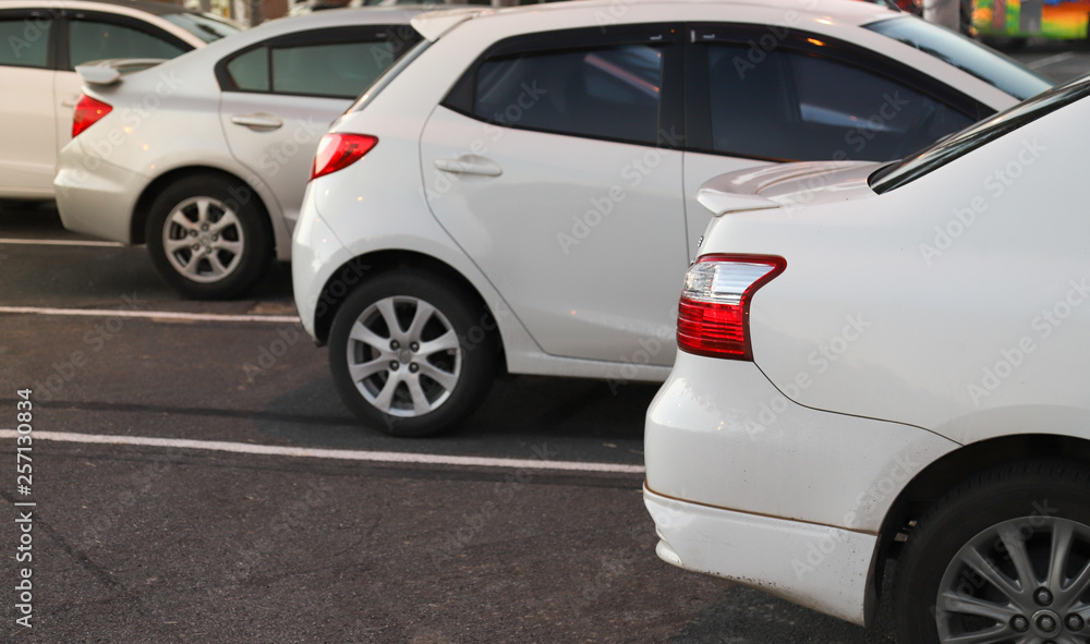 Closeup of rear or back side of white car with other cars parking in outdoor parking area in twilight evening.