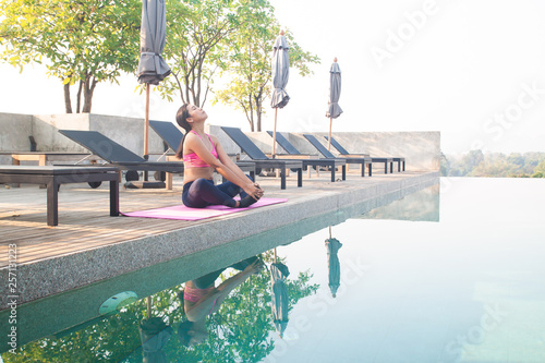 Healthy asian woman doing yoga at the poolside, roof top of hotel with beautiful view