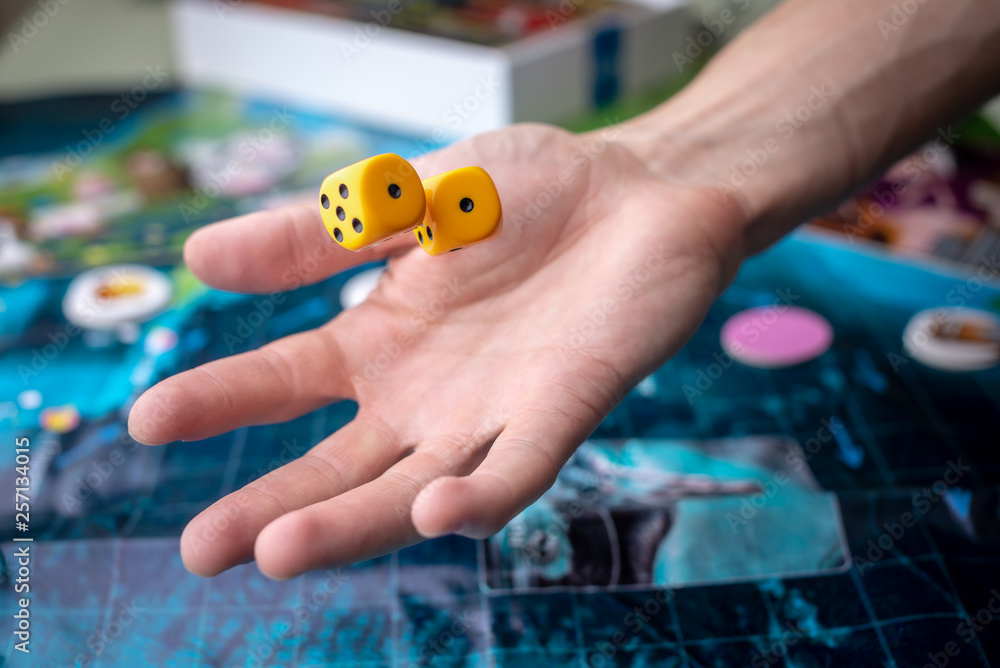Hand throws yellow dice on the playing field. Luck and excitement. Board games. Gaming moments in dynamics Hand throws yellow dice on the playing field. Luck and excitement. Board games. Gaming moments in dynamics