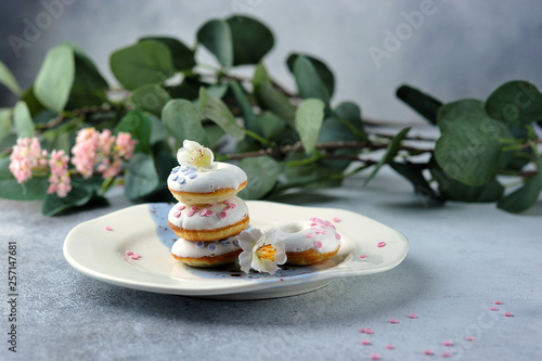 Donatos buns or donuts with icing on a plate. The composition is complemented by flowers and greens. Light background Close-up. photo