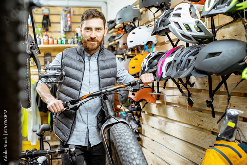 Portrait of a handsome man as a buyer or saleperson standing bicycle near the protective helmets at the bicycle shop