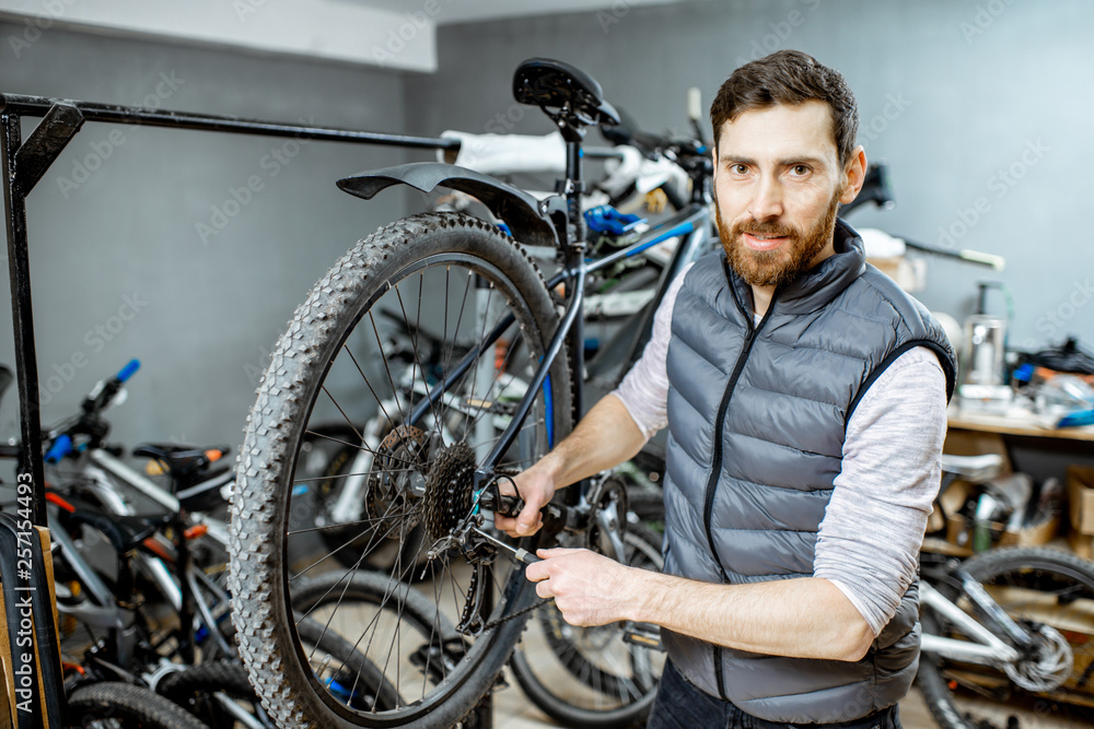 Handsome repairman serving a bicycle, fixing some malfunctions with gear selector at the workroom Handsome repairman serving a bicycle, fixing some malfunctions with gear selector at the workroom