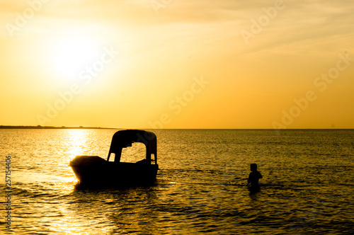 Silhouette of a man taking anchor for a boat with setting sun in the distance