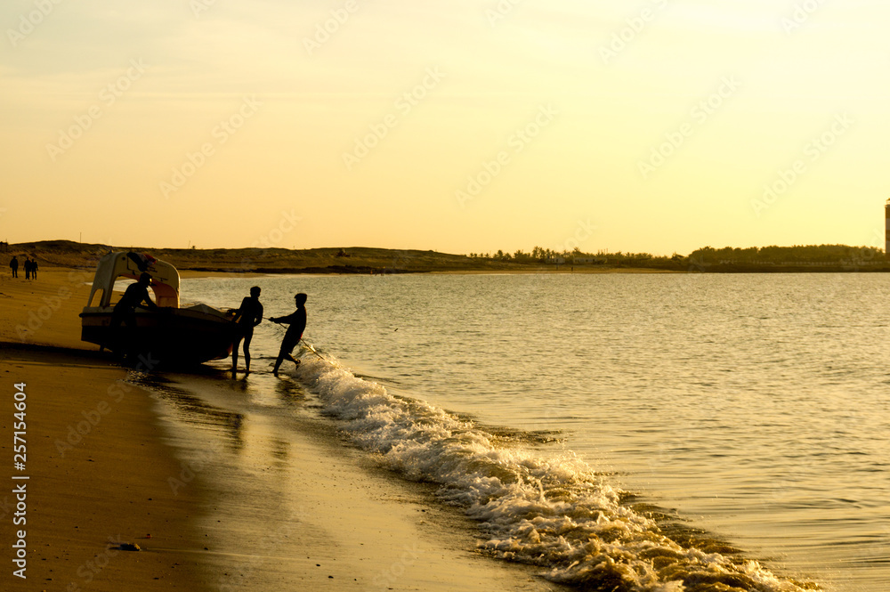 Silhouette of men pushing a tourist fishing boat into the ocean at a Gujarat beach