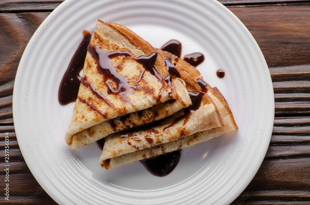 Flat lay French crepes with chocolate sauce in ceramic dish on wooden kitchen table Flat lay French crepes with chocolate sauce in ceramic dish on wooden kitchen table