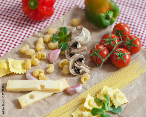 Cooking romantic italian dinner for two: fresh and healthy. Pasta, nice colorful vegetables, mushrooms and a bit of cheese. Served on a craft paper red tablecloth
