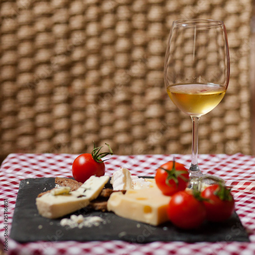 Delicious plate of french cheese served with fresh ripe tomatoes and bread on a black charcoal board. Red and white tablecloth for a picnic mood