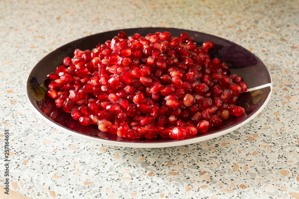 red ripe pomegranate seeds on a plate close-up. the fruit of pomegranate on a table with a marble texture red ripe pomegranate seeds on a plate close-up. the fruit of pomegranate on a table with a marble texture