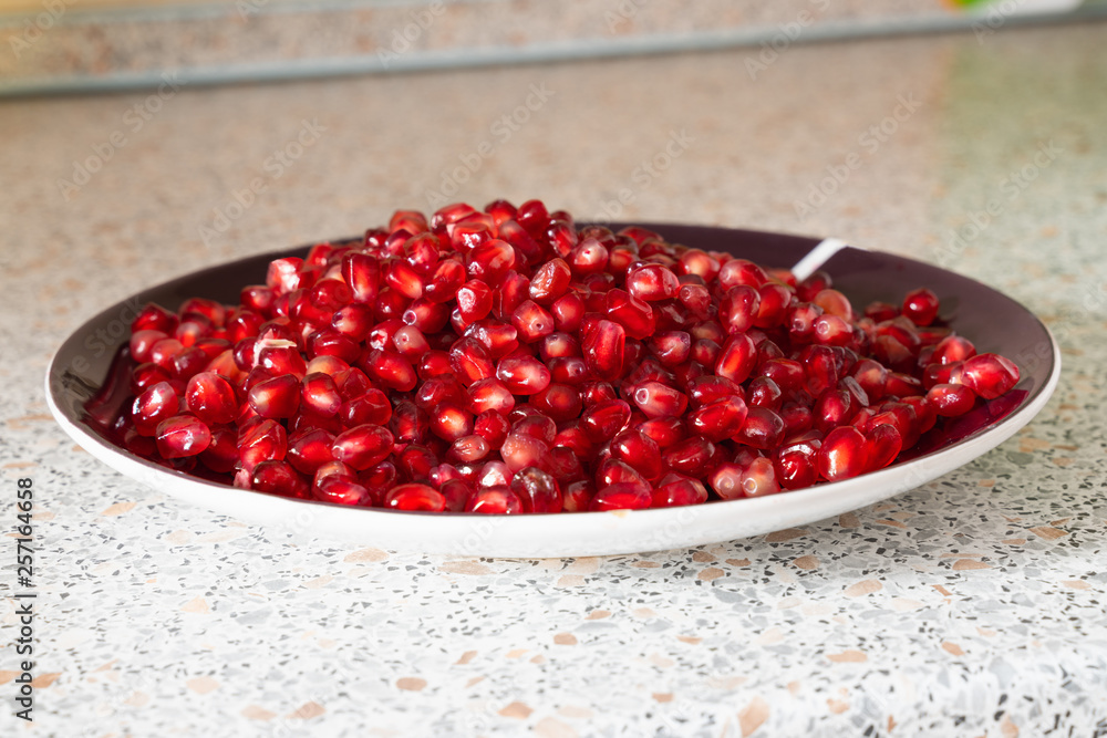 red ripe pomegranate seeds on a plate close-up. the fruit of pomegranate on a table with a marble texture red ripe pomegranate seeds on a plate close-up. the fruit of pomegranate on a table with a marble texture