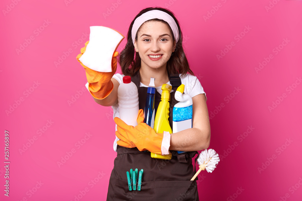 Close up portrait of smiling housekeeper woman holding bottles with cleaner liquid and show sponge. Charming female ready for cleaning her house, maid in high spirit, copy space for advertisment. Close up portrait of smiling housekeeper woman holding bottles with cleaner liquid and show sponge. Charming female ready for cleaning her house, maid in high spirit, copy space for advertisment.