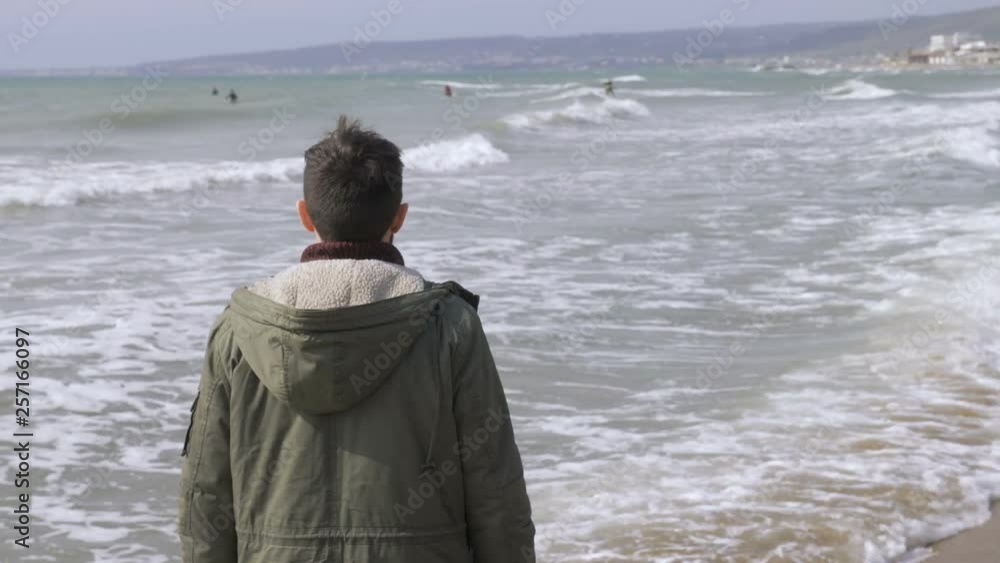 sad young man walking alone on the beach in winter windy day-back view sad young man walking alone on the beach in winter windy day-back view