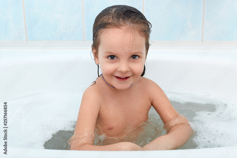 Cheerful happy toddler baby taking bath, suraunded foam bubbles. Little