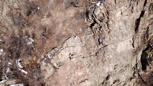 Climbers climb the rock. Drone footage. Side and top view. Rock lesson in the highlands. Gray rocks and dry bushes. Sometimes there is snow. Steep rock and cracks in places.