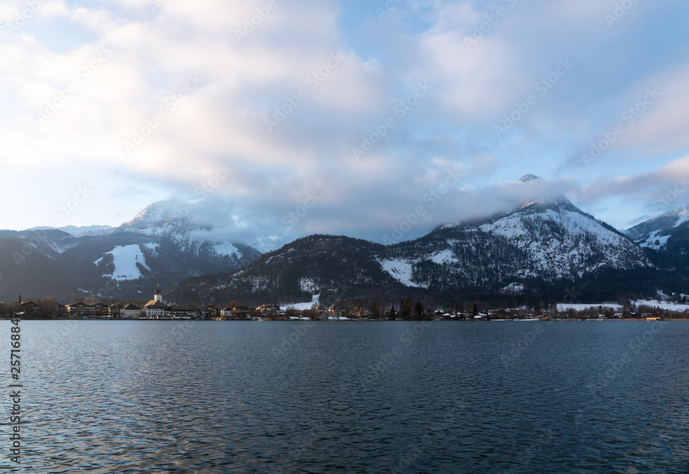 Wolfgangsee im Salzkammergut mit Strobl und schneebedeckten Bergen im Hintergrund, sonniger blauer Himmel mit weißen Wolken